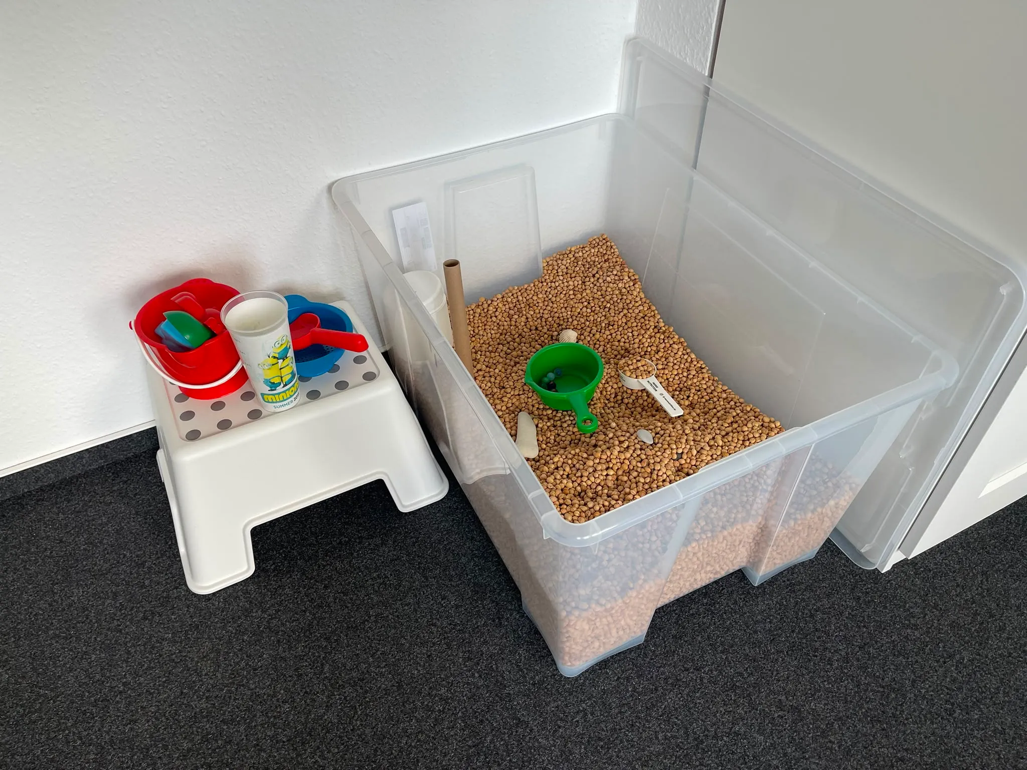 Kiste mit Körnern zum Fühlen, daneben Schaufeln und Becher